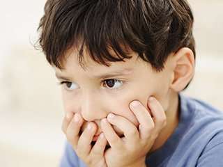 frustrated young boy holds face in hands